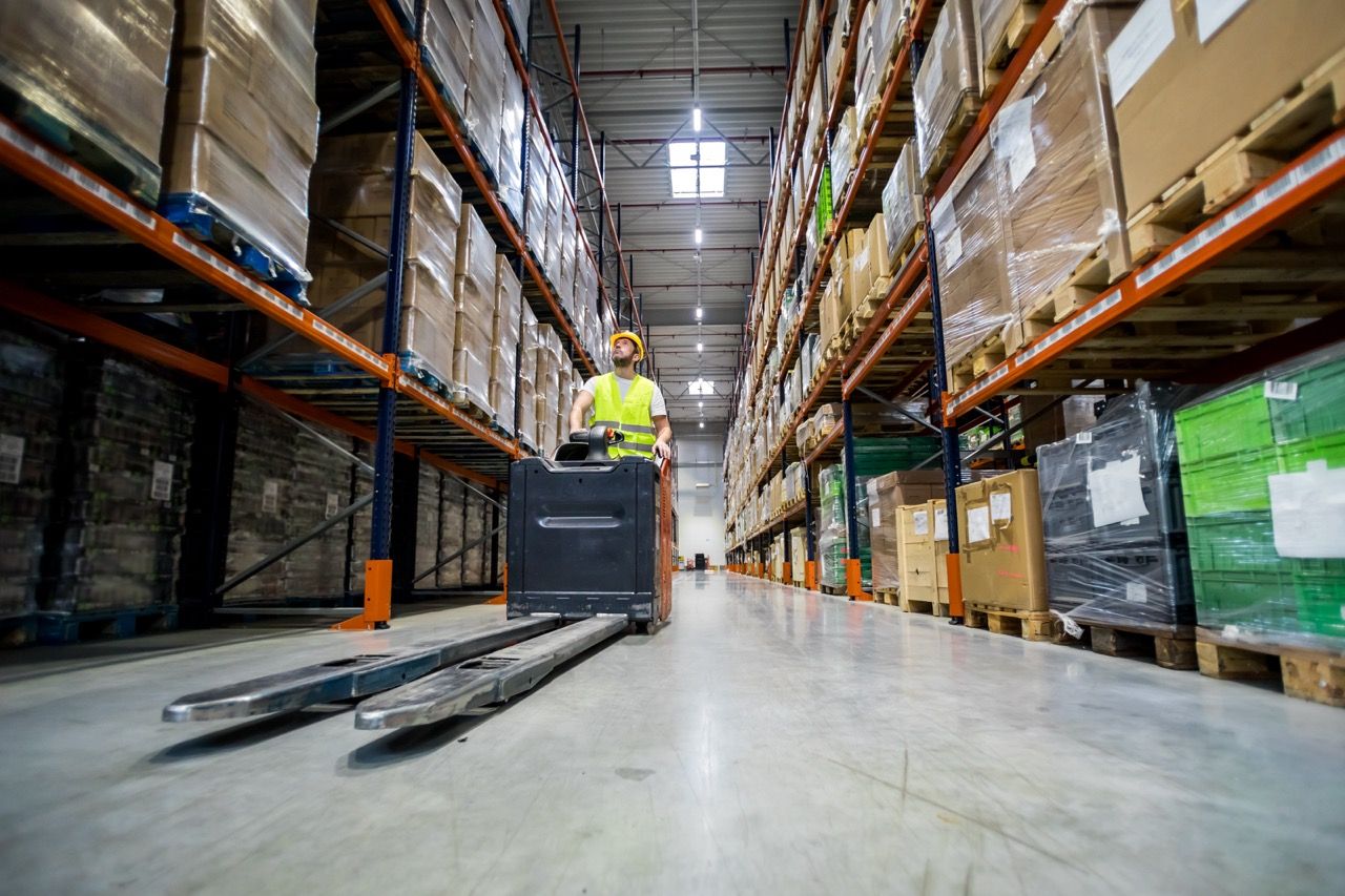 Forklift operator during work in large warehouse drives between shelves Avada Caterer Mobile App